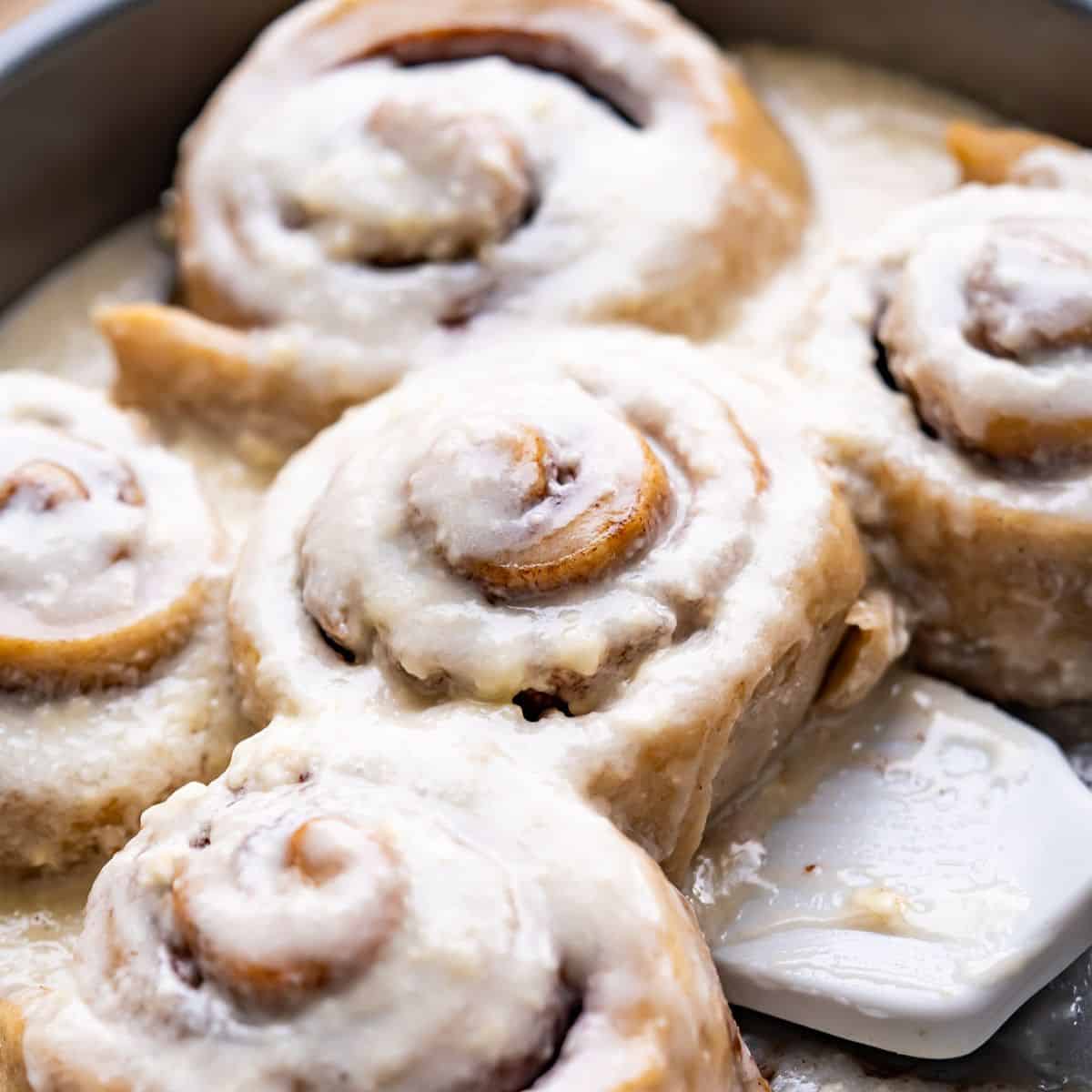 A pan of gooey gluten-free cinnamon rolls covered in vegan cream cheese frosting.