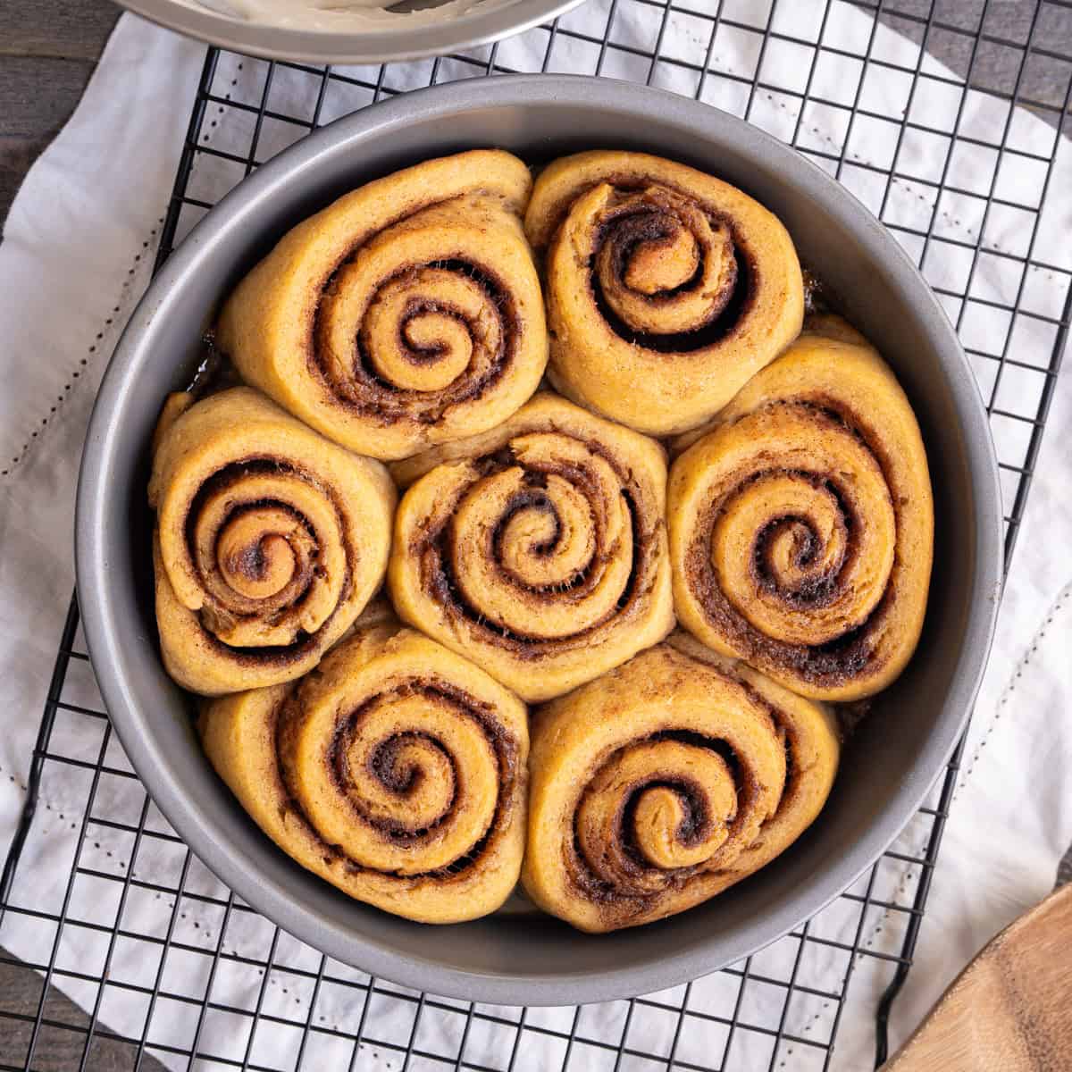 A round baking pan with 7 soft unfrosted gluten-free cinnamon rolls with perfect spirals.