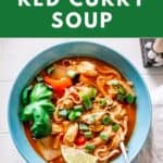 A bowl of red curry soup with rice noodles, chicken, and an assortment of toppings.