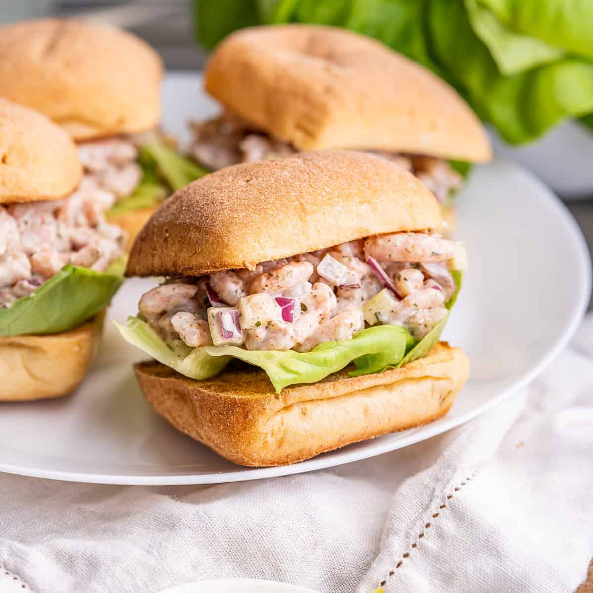 A side view of four loaded shrimp salad sandwiches on ciabatta.