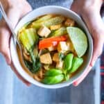 A bowl of Thai coconut curry soup with tofu and toppings.