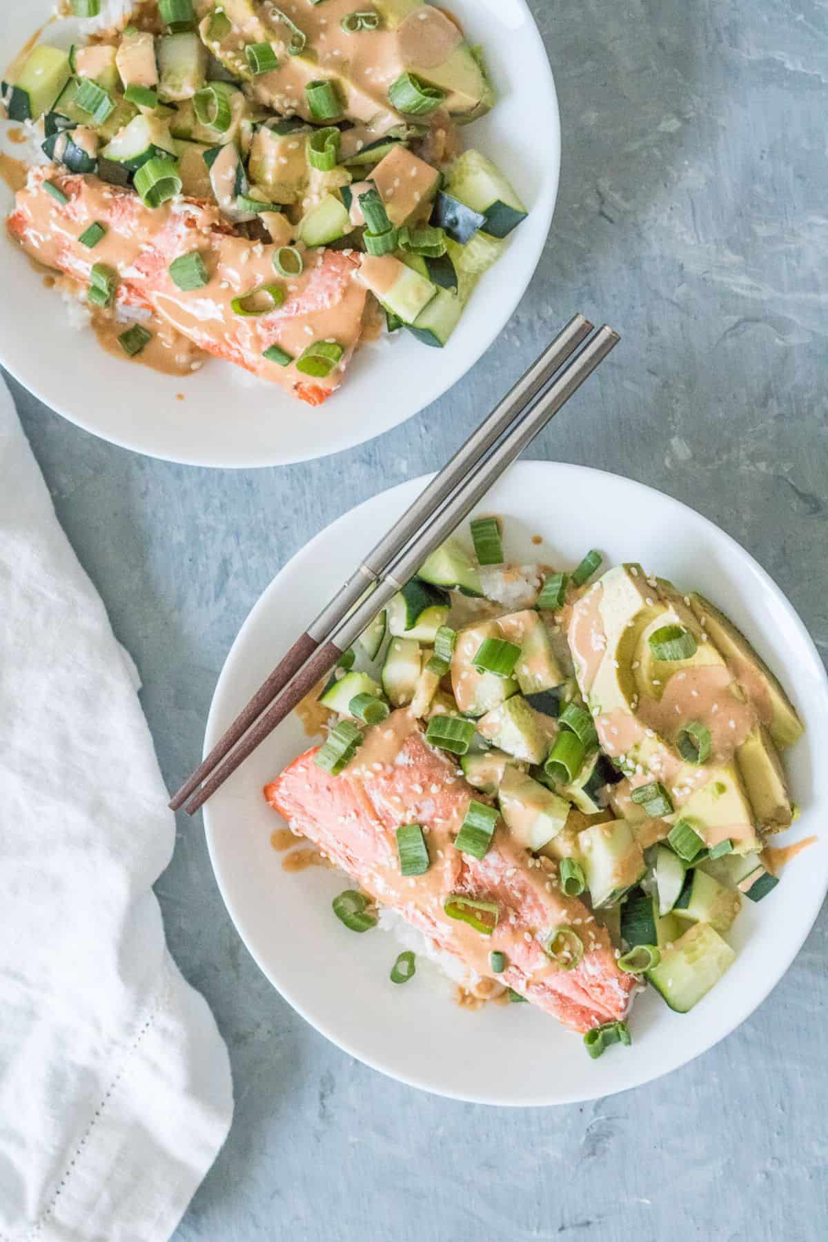 Two salmon sushi bowls with toppings and sriracha mayo, ready to eat.