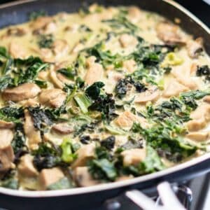 A close up of a pan of green pork curry with kale and mushroom in a creamy coconut sauce.