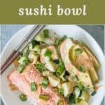 A salmon sushi bowl with cooked salmon, cucumber, avocado, green onions, rice and a sriracha mayo sauce.