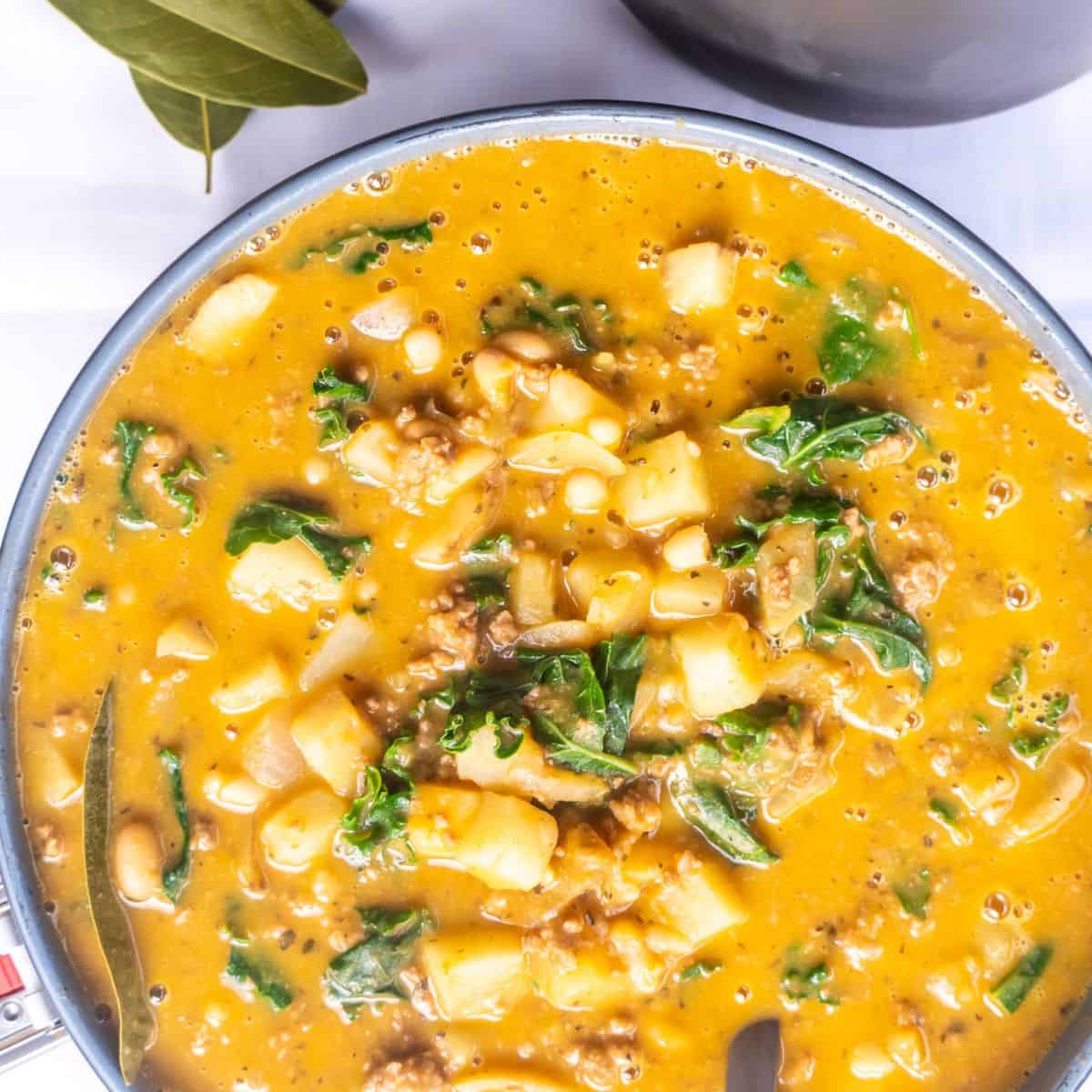 A pot of savory pumpkin stew with potatoes, beans, and kale.