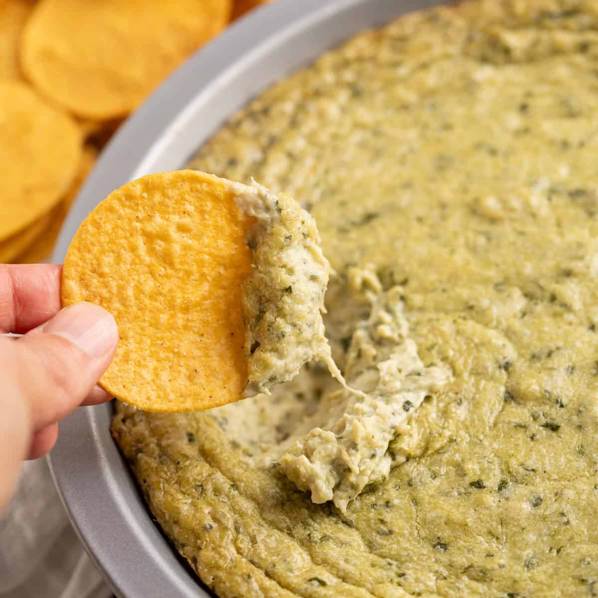 A chip dipped into creamy and chunky dairy-free spinach artichoke dip.