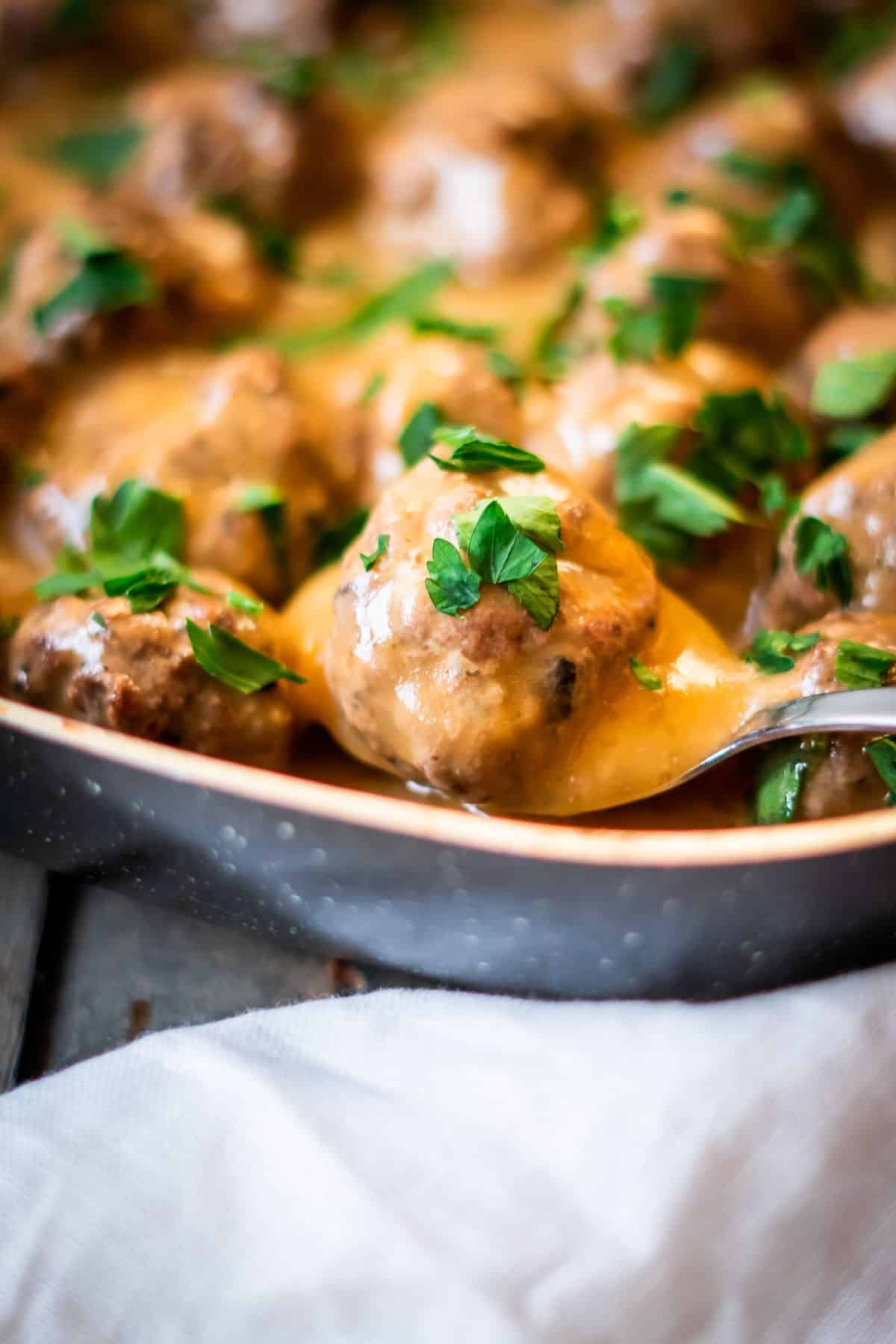 A close up of a dairy-free Swedish meatball on a spoon, garnished with fresh parsley.