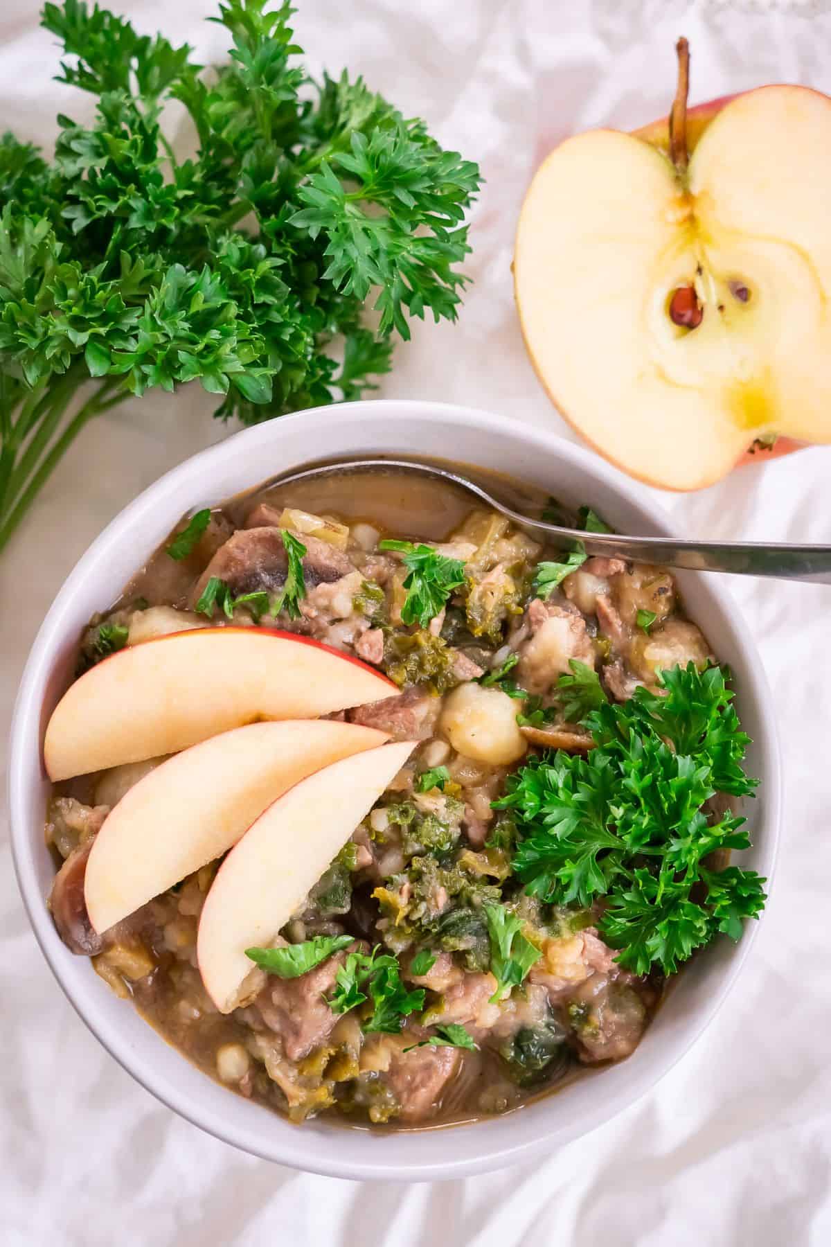 A bowl of Instant Pot Beef Stew topped with apple slices and parsley.