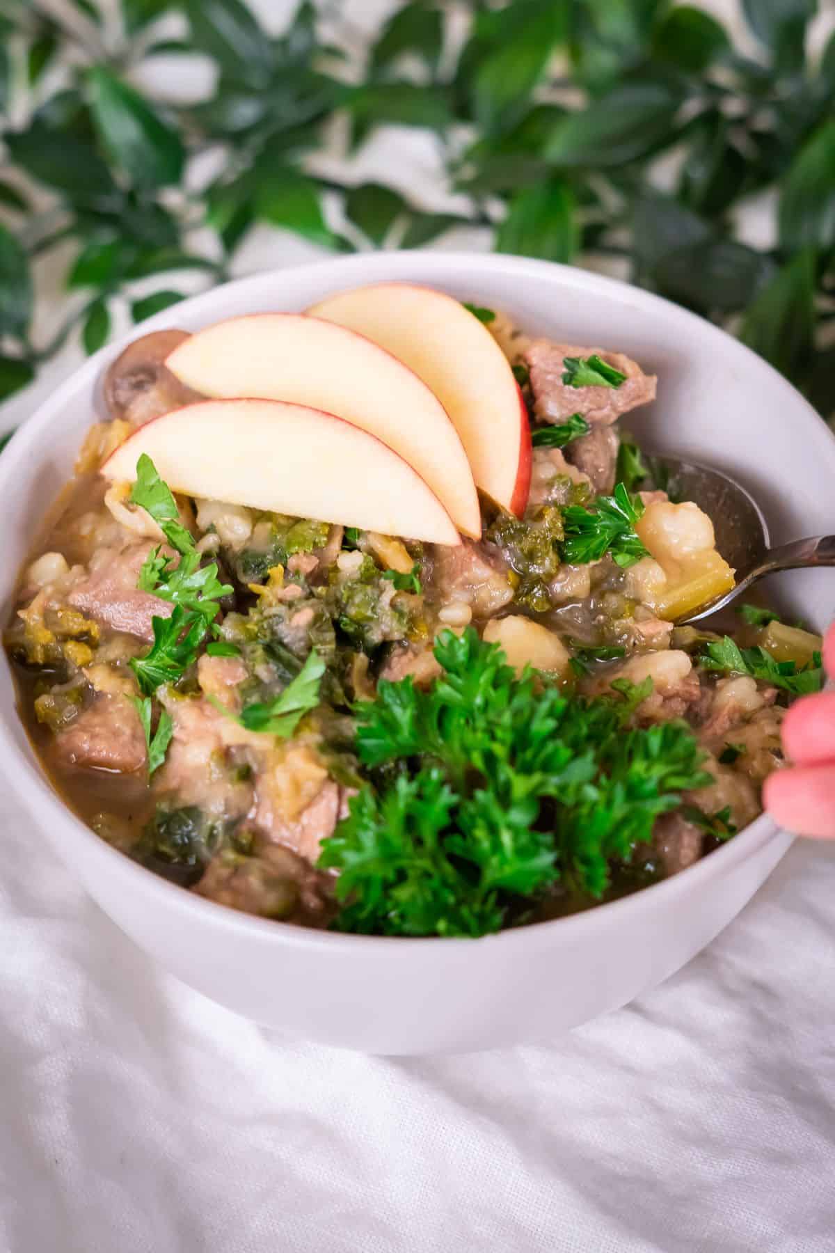 A bowl of Instant Pot Beef stew topped with some fresh apple slices and parsley.