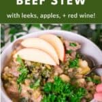 A thick and hearty bowl of Instant Pot Beef Stew loaded with vegetables and topped with apple slices and a sprig of parsley.
