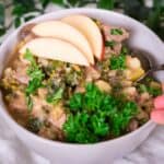 A thick and hearty bowl of Instant Pot Beef Stew loaded with vegetables and topped with apple slices and a sprig of parsley.