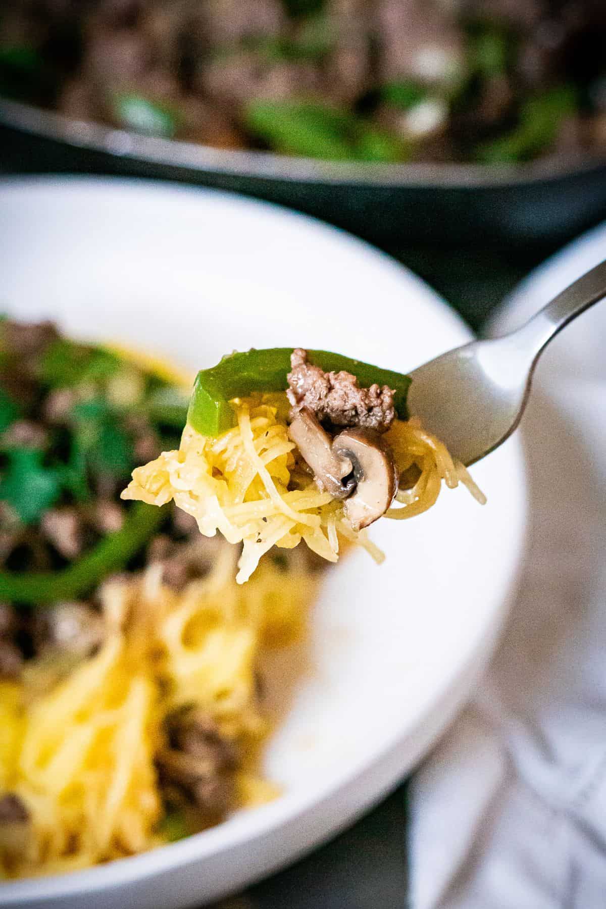 A forkful of spaghetti squash, ground beef, a slice of green pepper and a mushroom piece.
