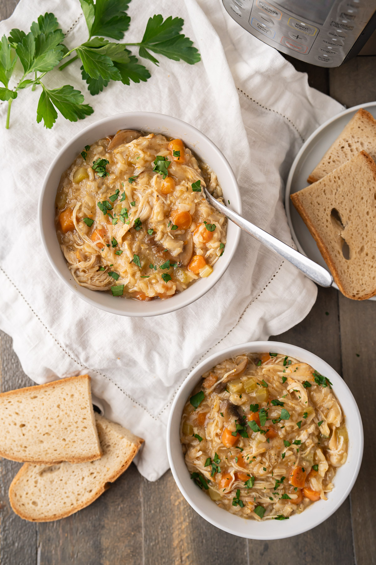 A table spread with two bowls of Instant Pot Chicken and Rice Soup and slices of toasted gluten-free bread with the Instant Pot.