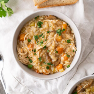A serving bowl of Instant Pot chicken and rice soup with chopped parsley to garnish.