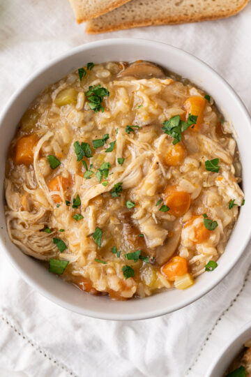 A serving bowl of Instant Pot chicken and rice soup with chopped parsley to garnish.