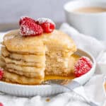 A stack of four fluffy gluten-free pancakes with maple syrup and fresh raspberries.