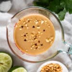 A liquid measuring cup filled with freshly made Thai peanut butter sauce and sprinkled with crunchy crushed peanuts.