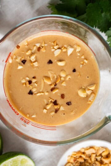A liquid measuring cup filled with freshly made Thai peanut butter sauce and sprinkled with crunchy crushed peanuts.