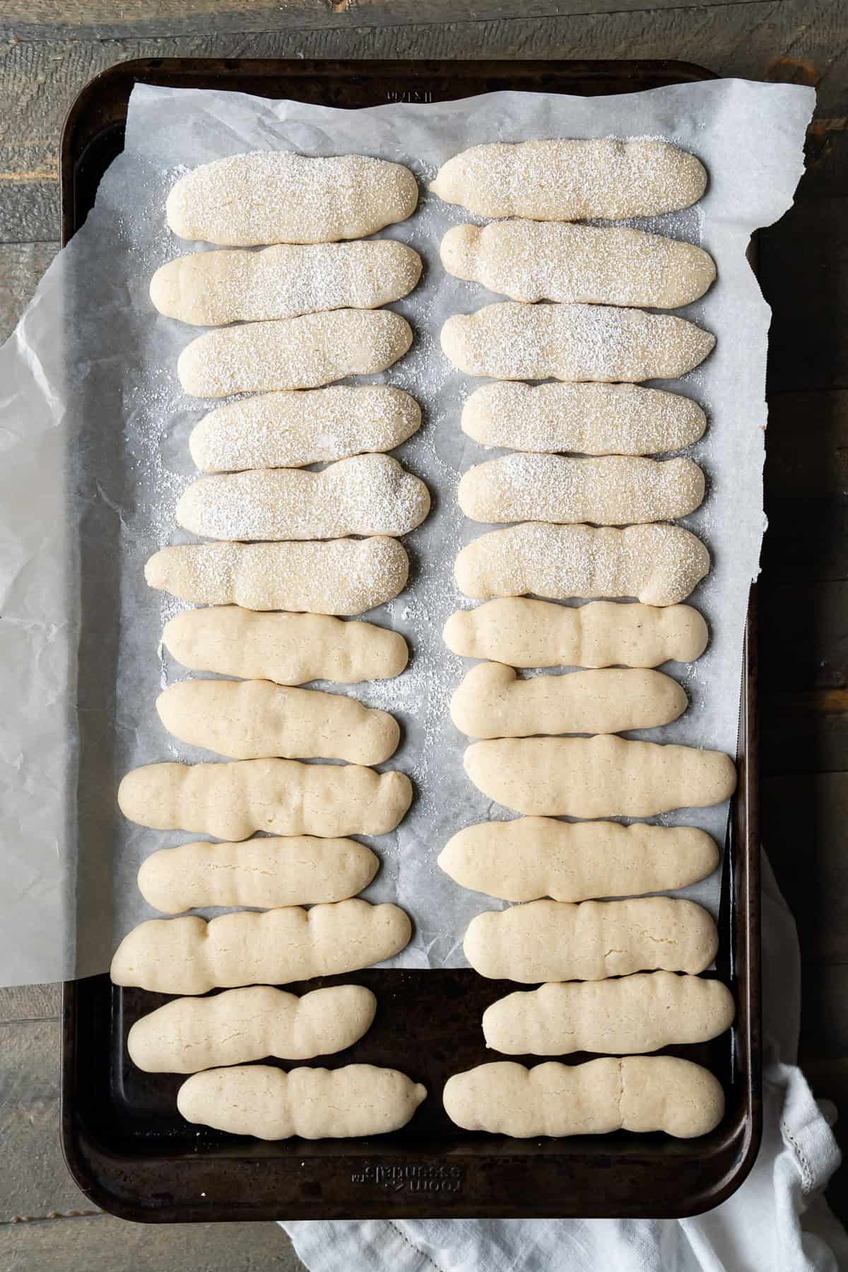 A full set of 26 soft vegan ladyfinger cookies arranged to cool on a baking sheet.