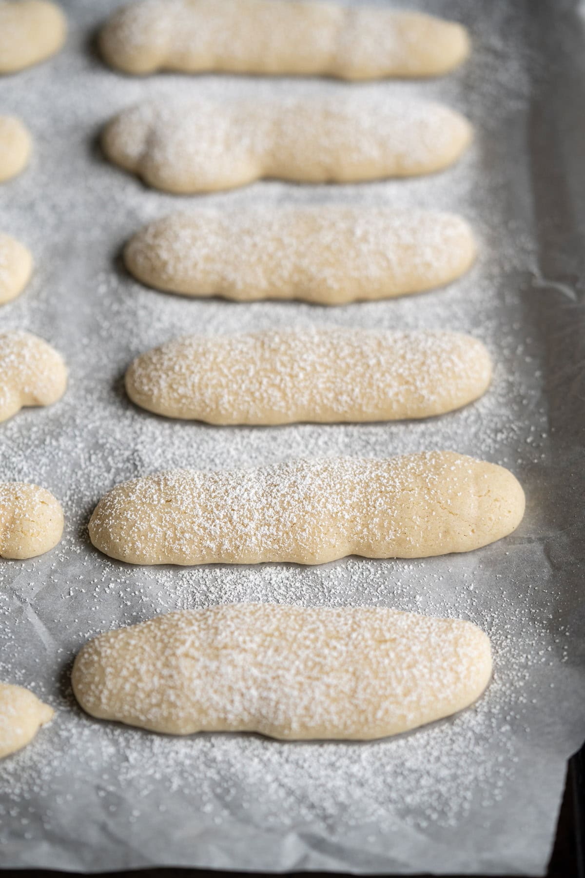 A close up of soft vegan ladyfinger sponge cookies dusted with powdered sugar.