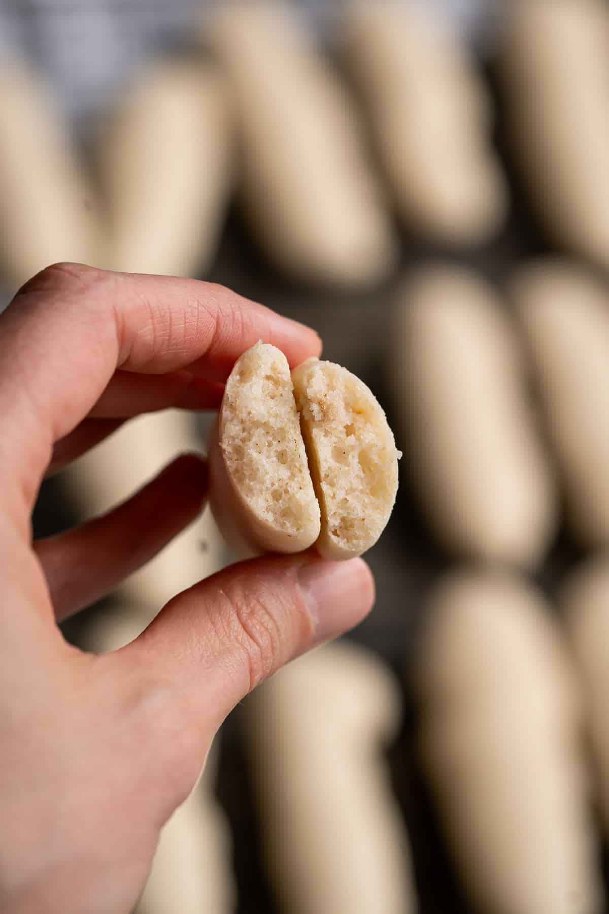 A vegan ladyfinger broken in half to show the light and spongy inside.