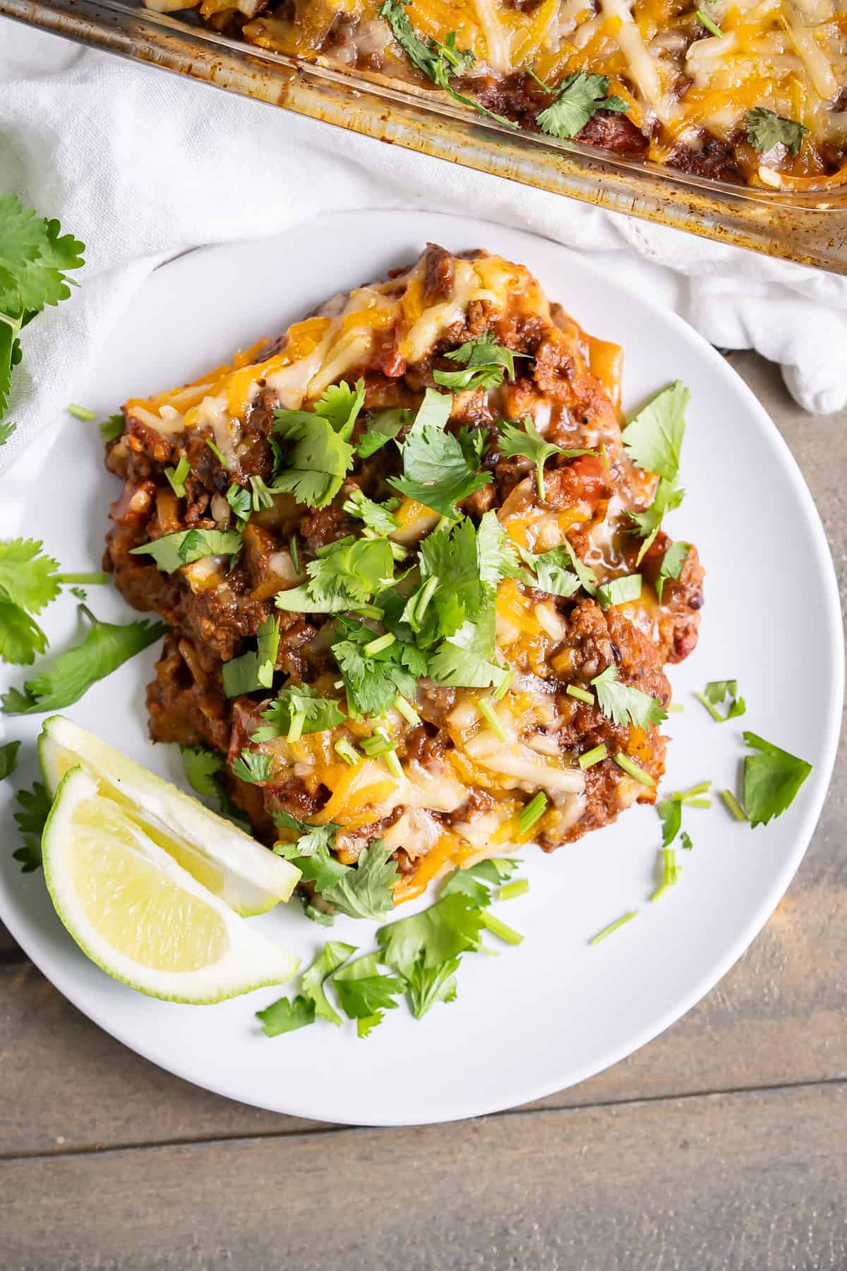A serving of enchilada casserole on a plate topped with chopped cilantro and lime wedges.