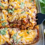 Lifting a slice of enchilada casserole out of the baking dish with a spatula.