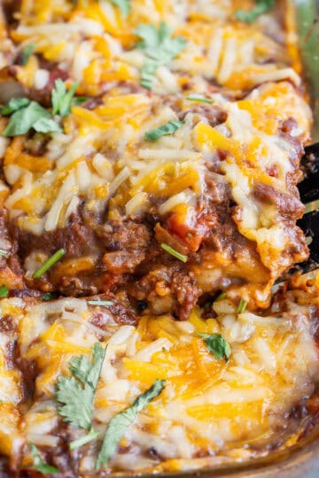 Lifting a slice of enchilada casserole out of the baking dish with a spatula.