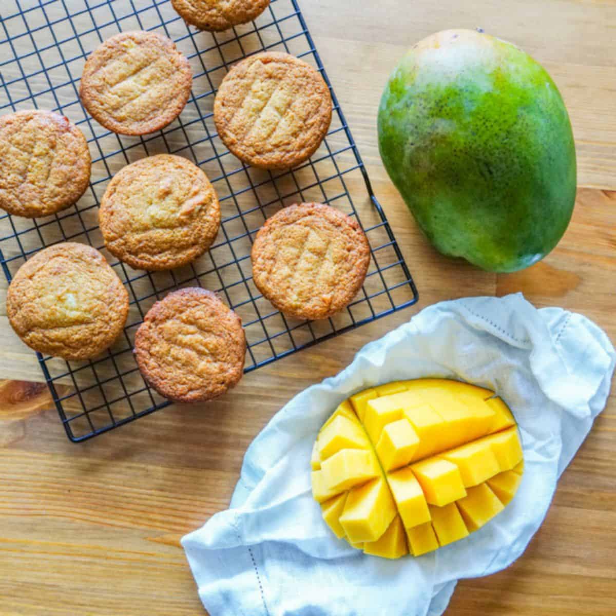 A batch of mango muffins beside a fresh cut mango.