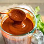 A spoon dripping homemade enchilada sauce into a liquid measuring cup to show the thickness.