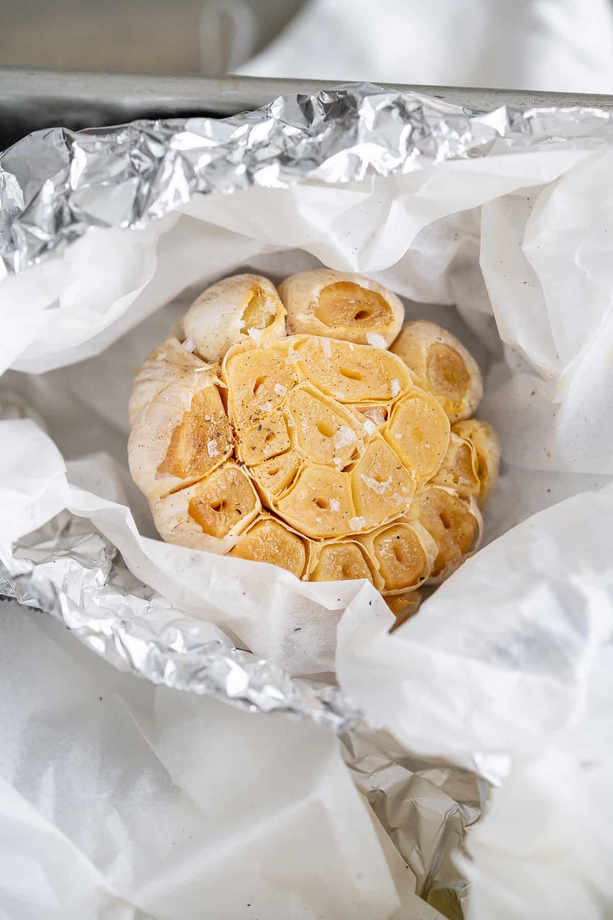 A roasted garlic head nestled in parchment paper and foil.