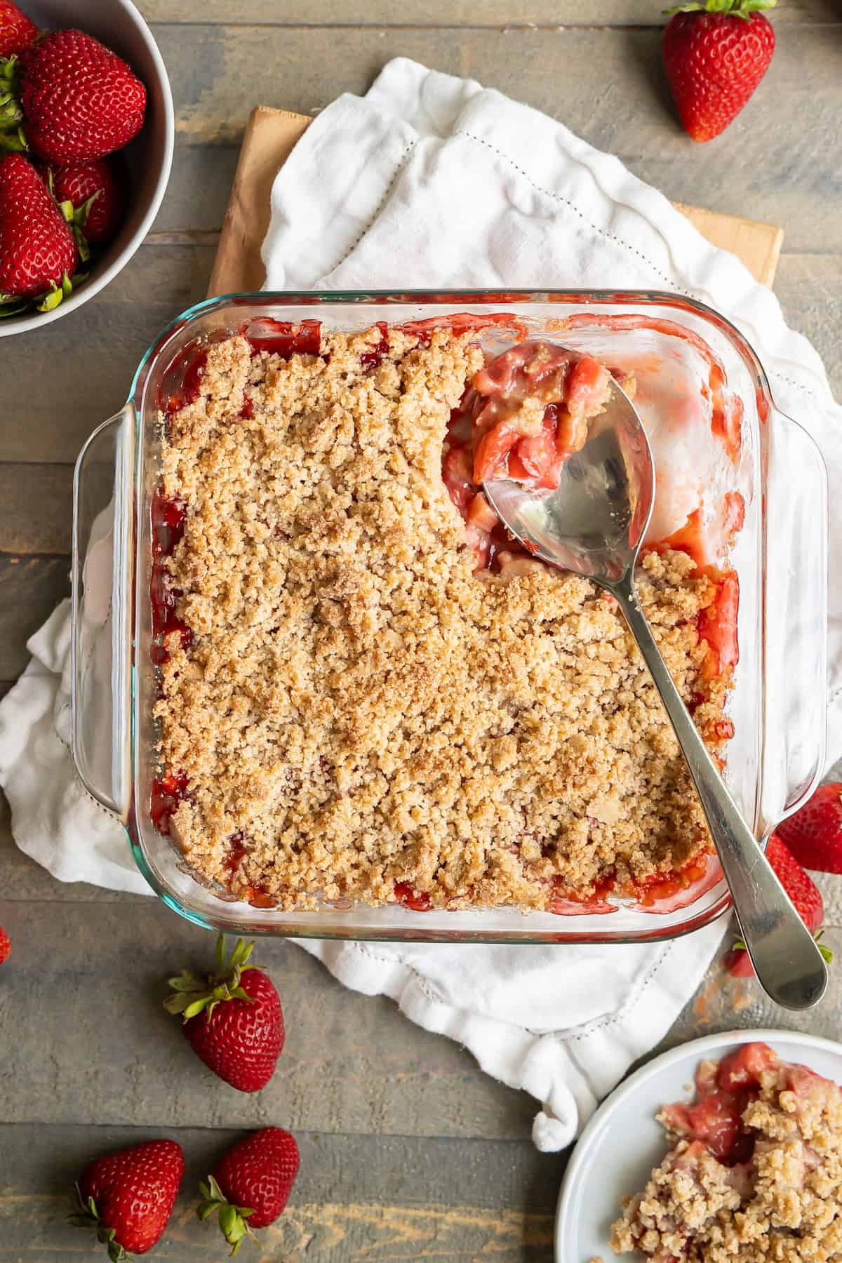 The dish of strawberry rhubarb crumble with a piece removed to show the glazed filling and crispy crumble topping.