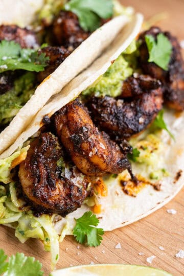 The inside of blackened shrimp tacos featuring avocado slaw, shrimp, cilantro, and flaky sea salt.