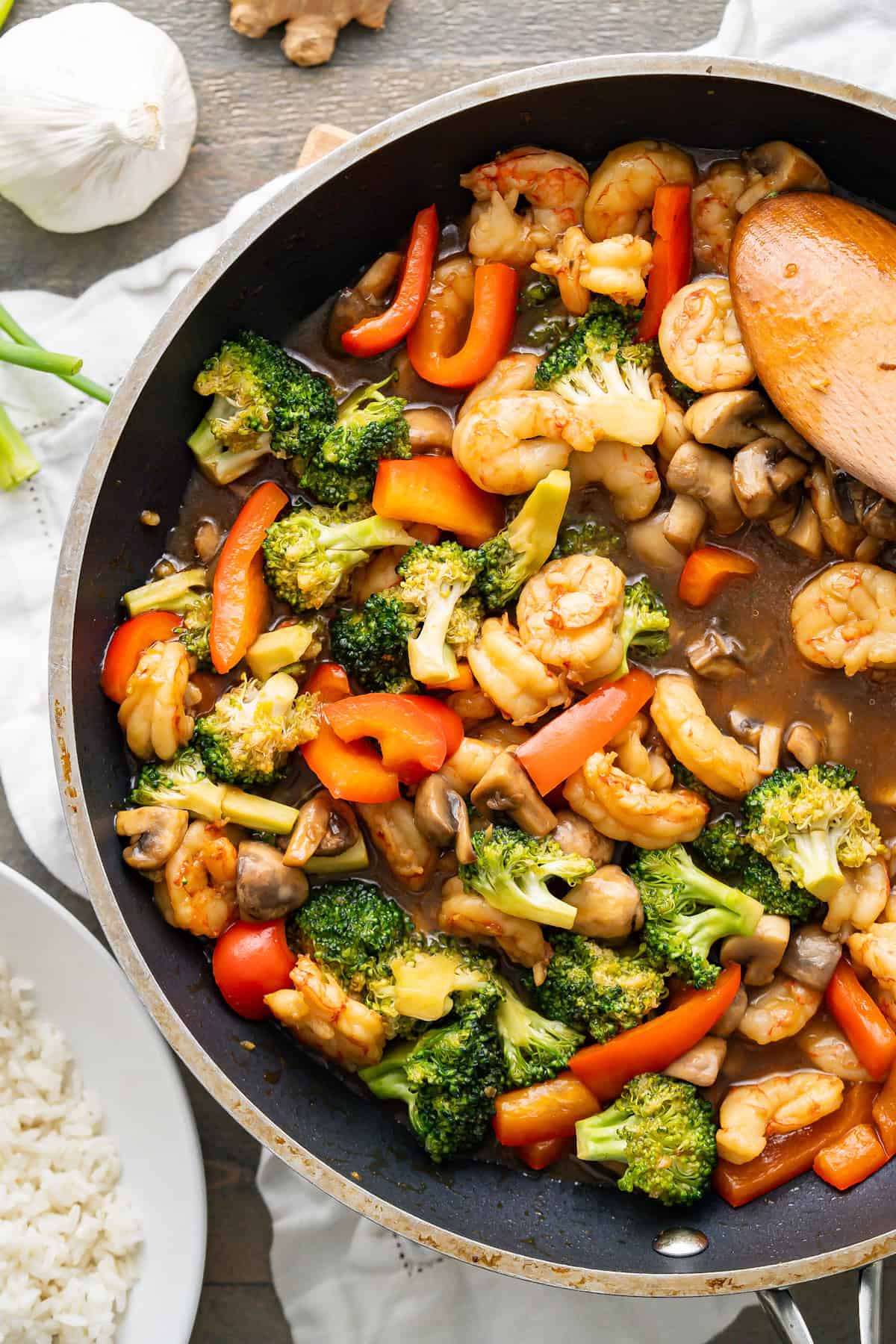 A large skillet filled with shrimp, broccoli, red bell peppers, mushrooms, and stir fry sauce.