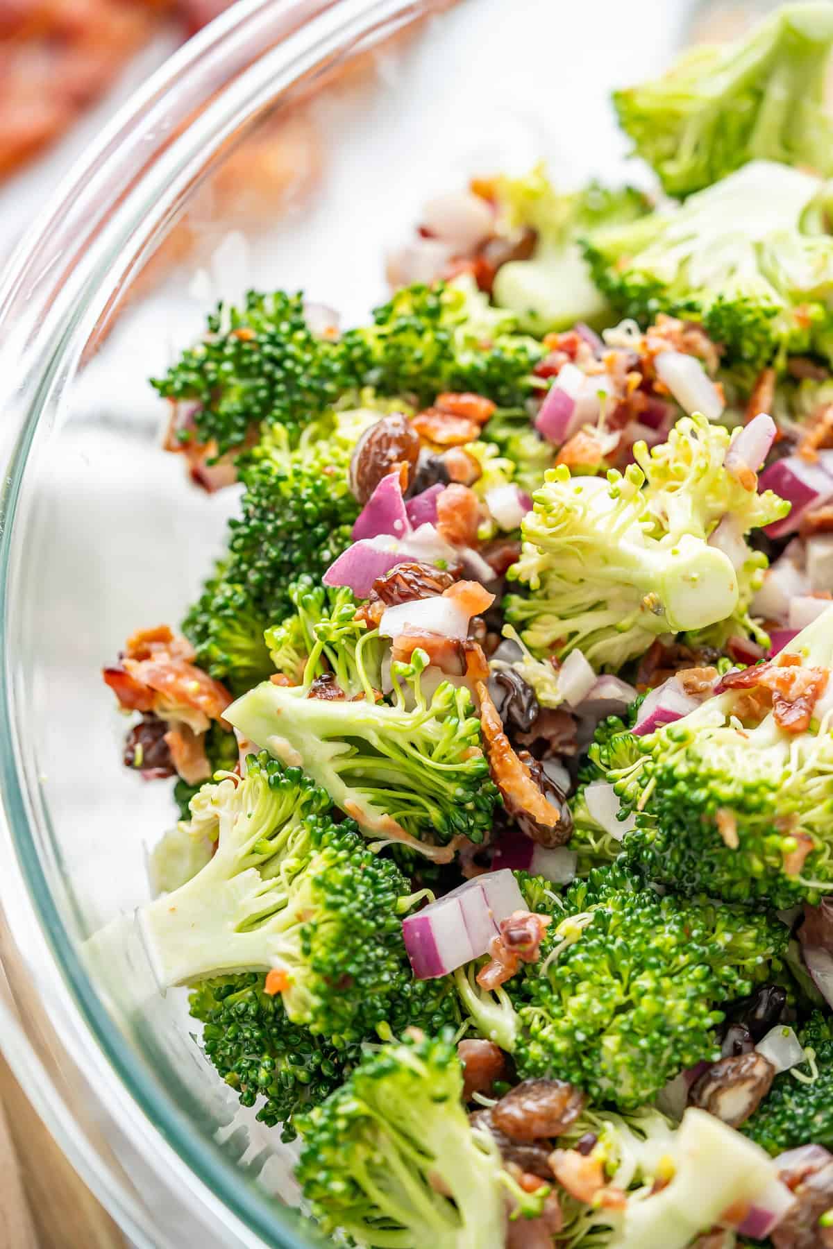 A serving bowl of broccoli salad with finely chopped red onions and crispy bacon.