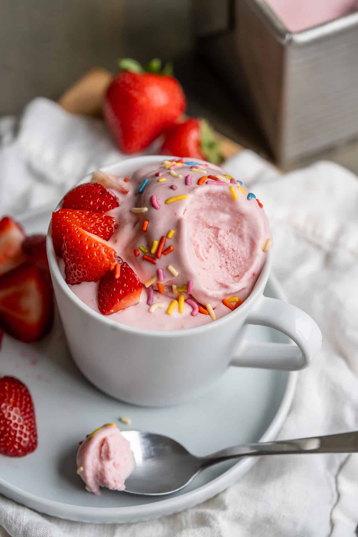 A cup of dairy-free strawberry ice cream with a bit removed to show the creamy classic ice cream texture.