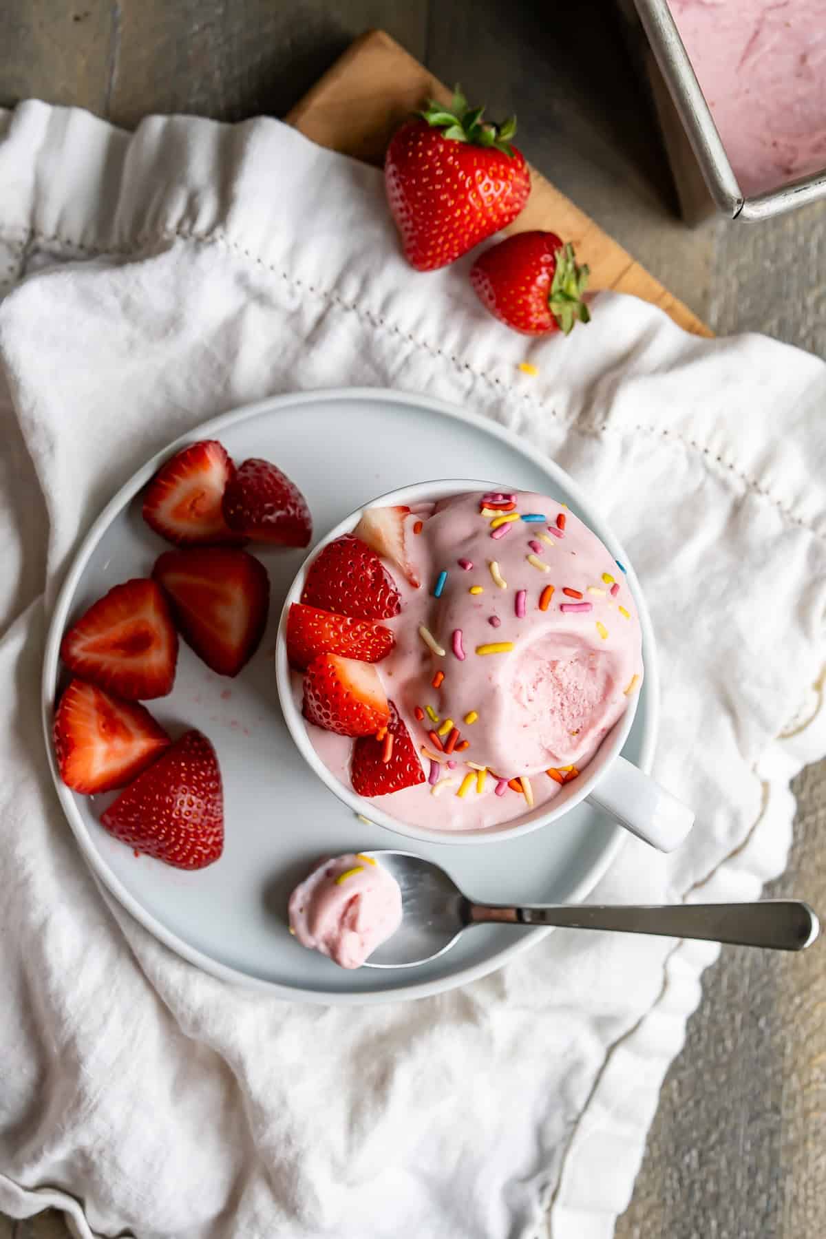 A place setting of strawberry ice cream with sprinkles and chopped strawberry pieces.