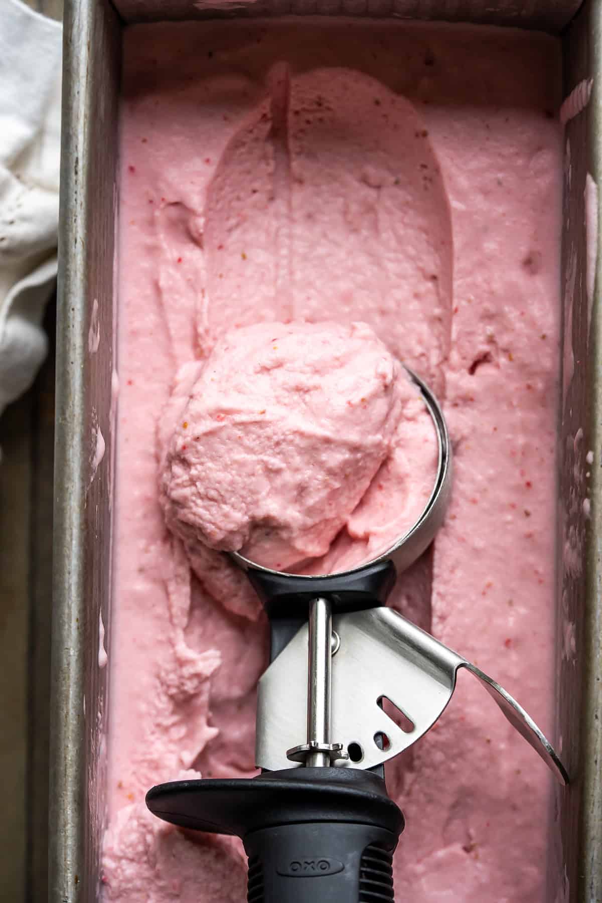 Scooping creamy dairy-free strawberry ice cream with a scoop.