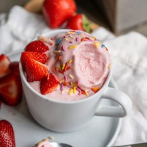 A cup of dairy-free strawberry ice cream with a bit removed to show the creamy classic ice cream texture.