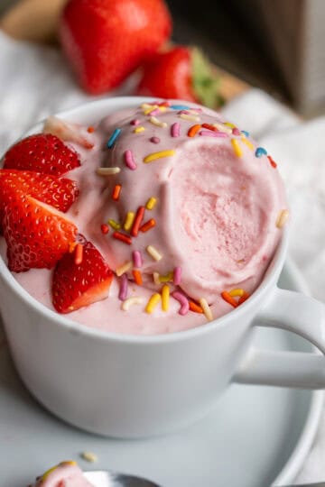 A cup of dairy-free strawberry ice cream with a bit removed to show the creamy classic ice cream texture.
