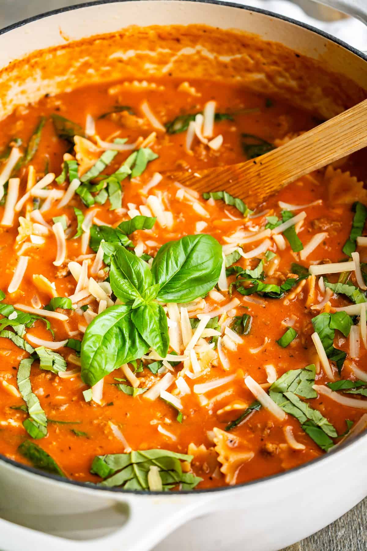 A pot of lasagna soup garnished with an extra sprinkle of mozzarella cheese and fresh basil leaves.