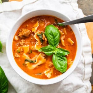 A serving bowl of lasagna soup topped with fresh basil leaves.