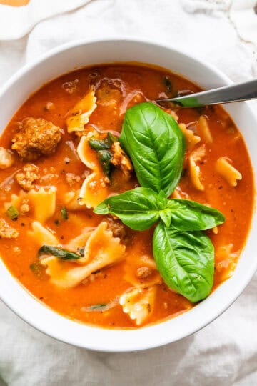 A serving bowl of lasagna soup topped with fresh basil leaves.