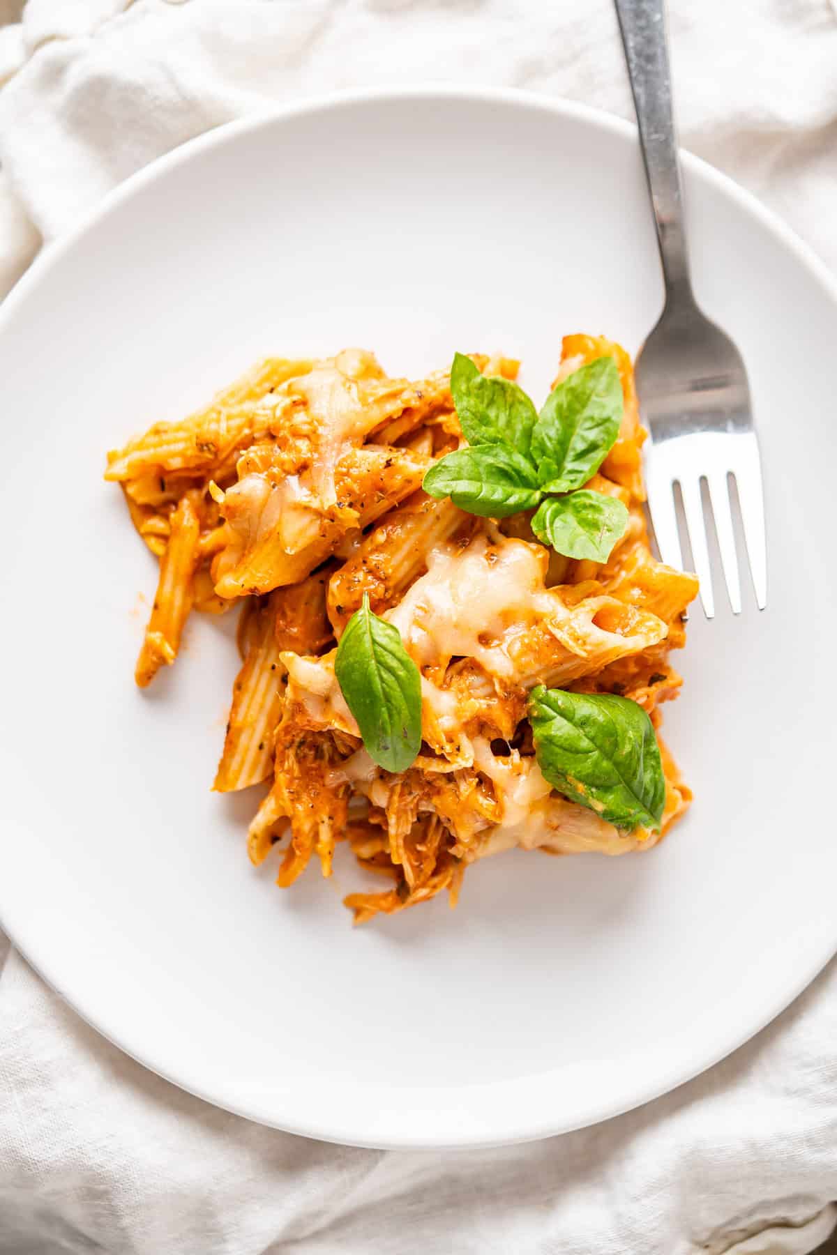 A close up of a plate with leftover turkey baked ziti with fresh basil leaves to garnish.