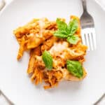 A close up of a plate with leftover turkey baked ziti with fresh basil leaves to garnish.