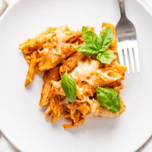A close up of a plate with leftover turkey baked ziti with fresh basil leaves to garnish.