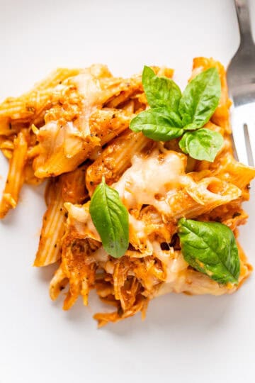 A close up of a plate with leftover turkey baked ziti with fresh basil leaves to garnish.