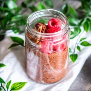 A jar of chocolate chia pudding topped with raspberries and pecans.