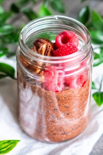 A jar of chocolate chia pudding topped with raspberries and pecans.