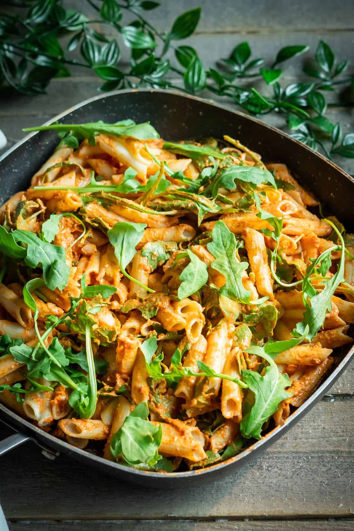 A serving pan of sun-dried tomato pasta mixed with fresh arugula.